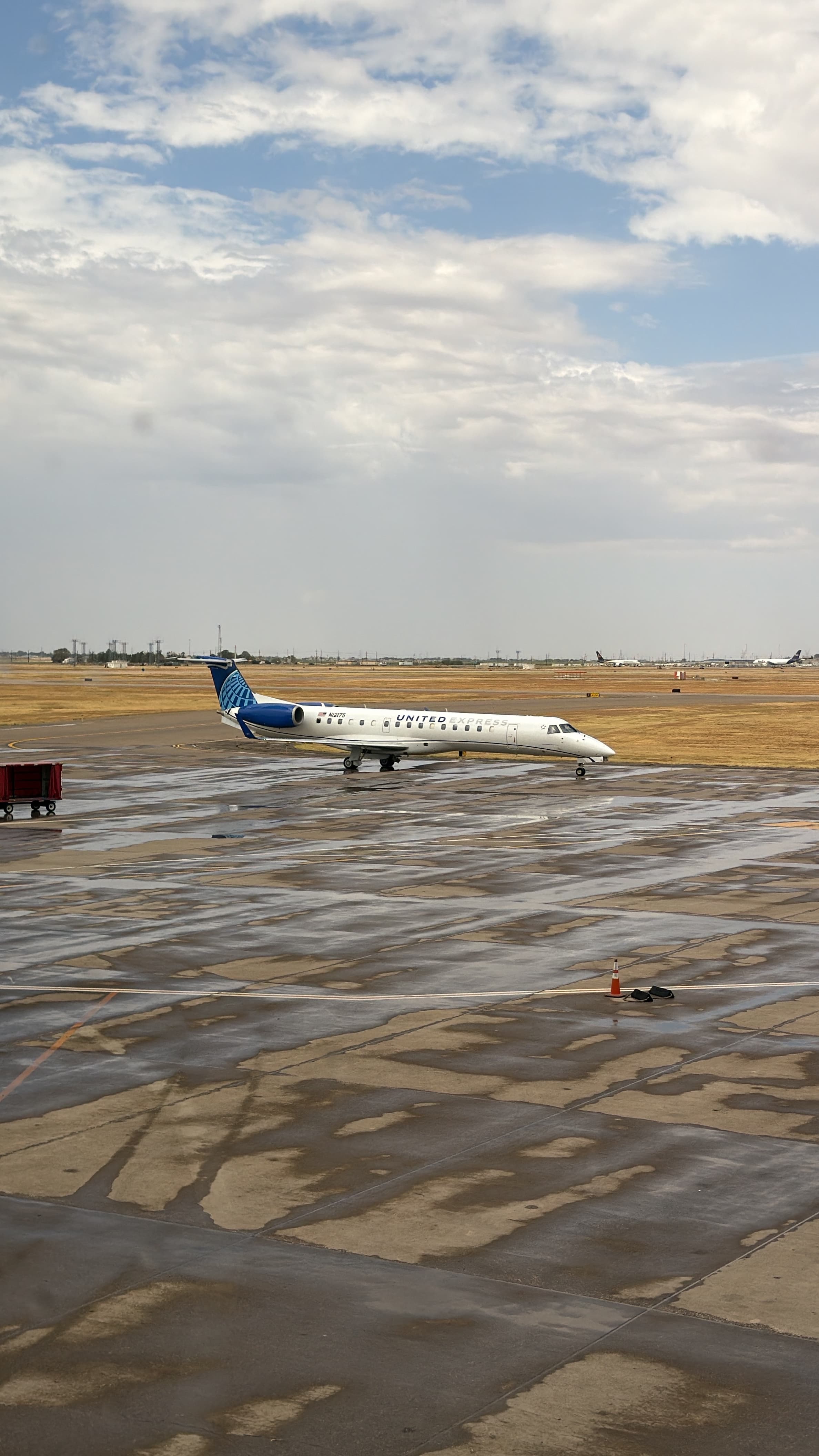 United Express Embraer N12175 on a wet apron beneath broken cloud