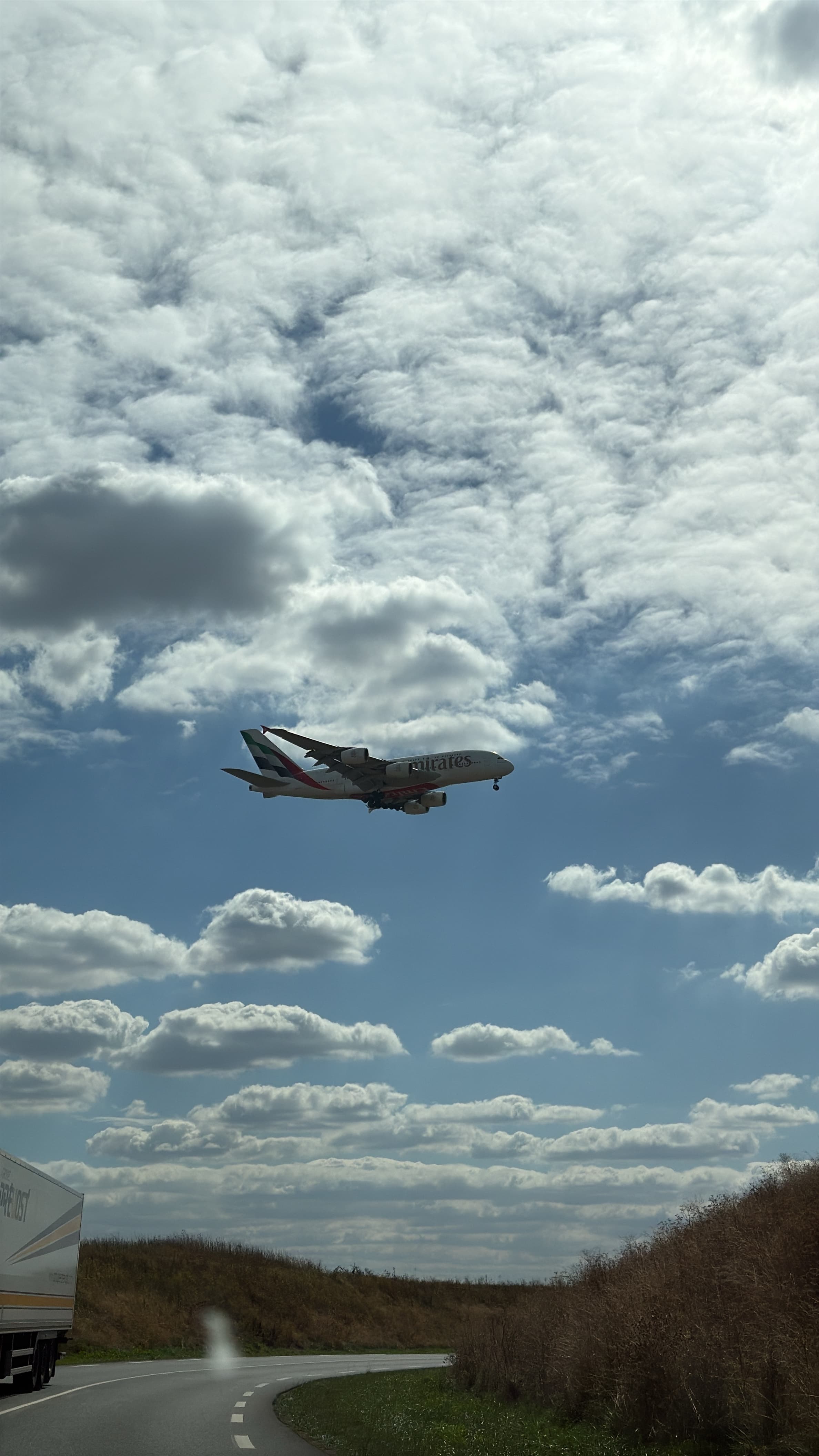 Emirates Airbus A380 A6-EOK flying above a road beneath textured cloud