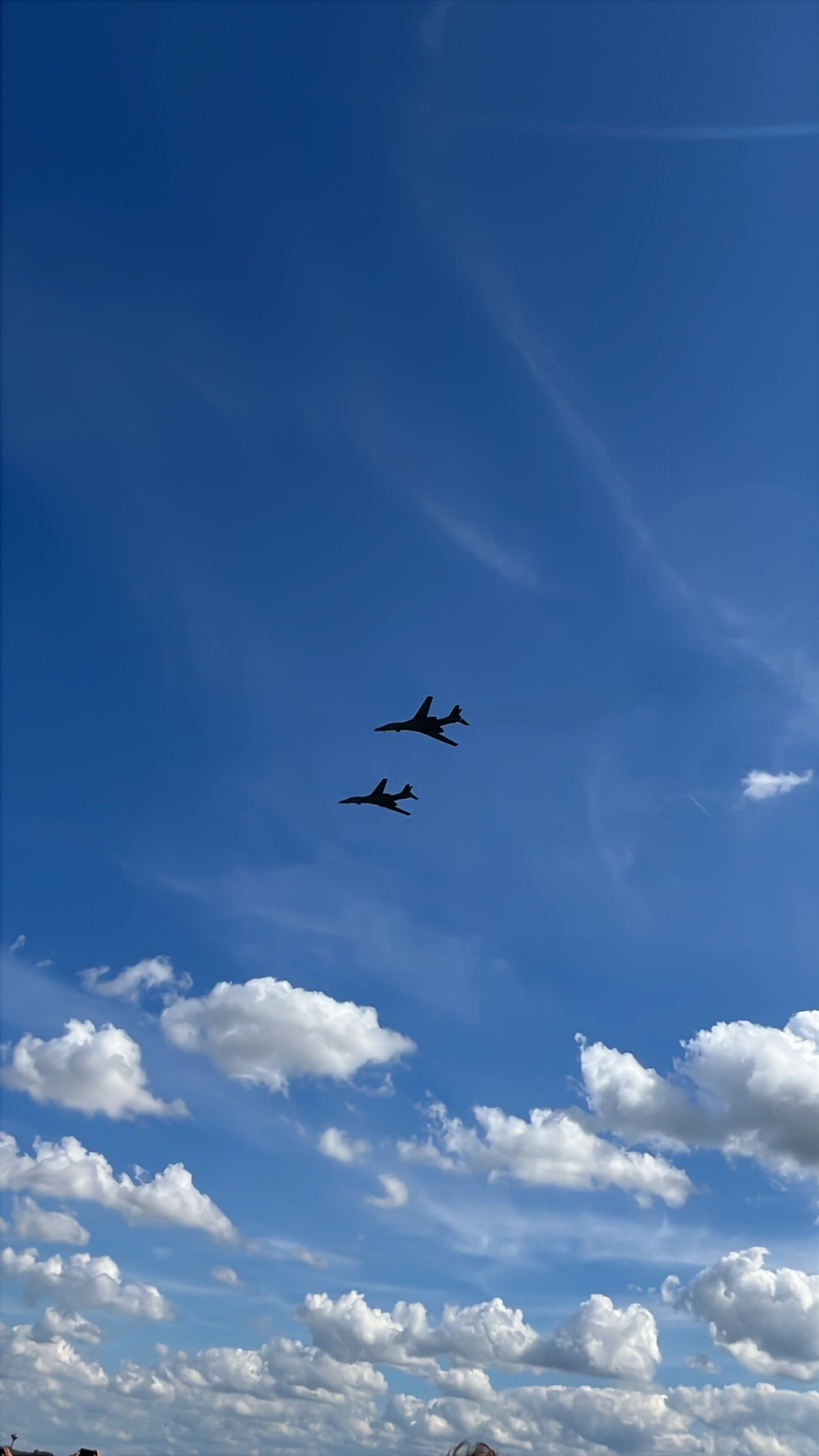 Two B-1 Lancer silhouettes crossing a blue sky above bright clouds